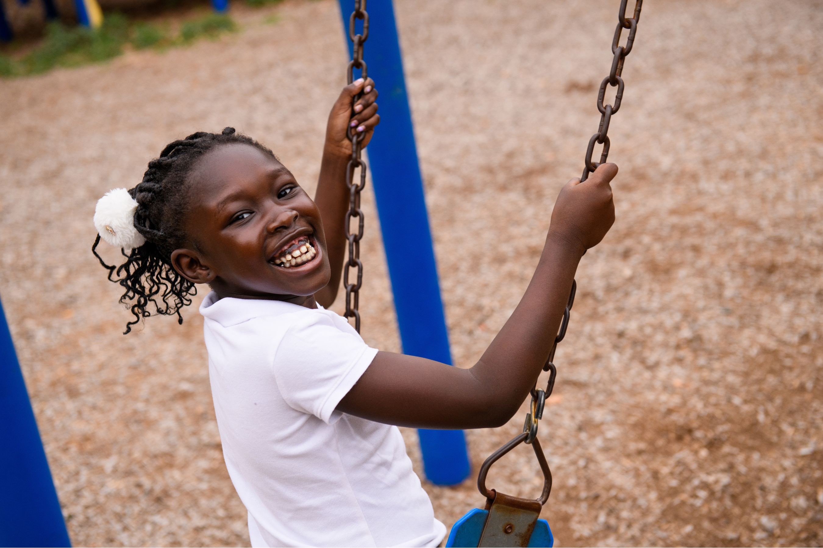 a young girl on a swing set smiling over her shoulder to look at the camera