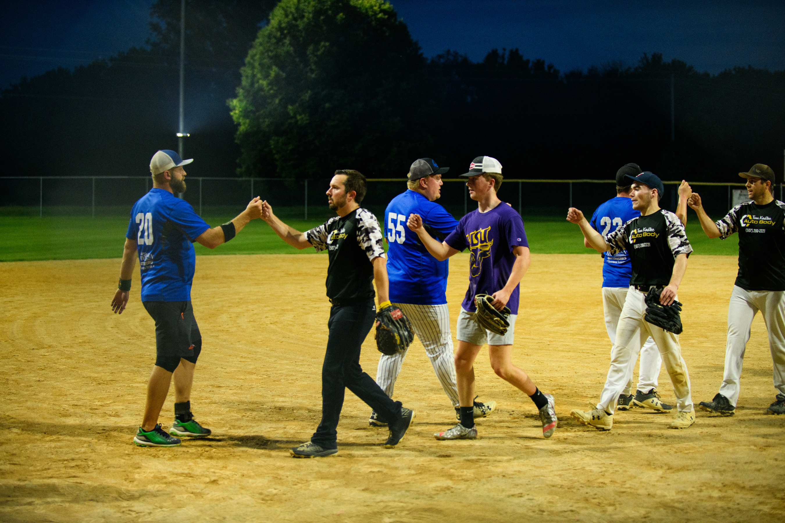 two teams of softball players exchanging fist bumps on the field at night