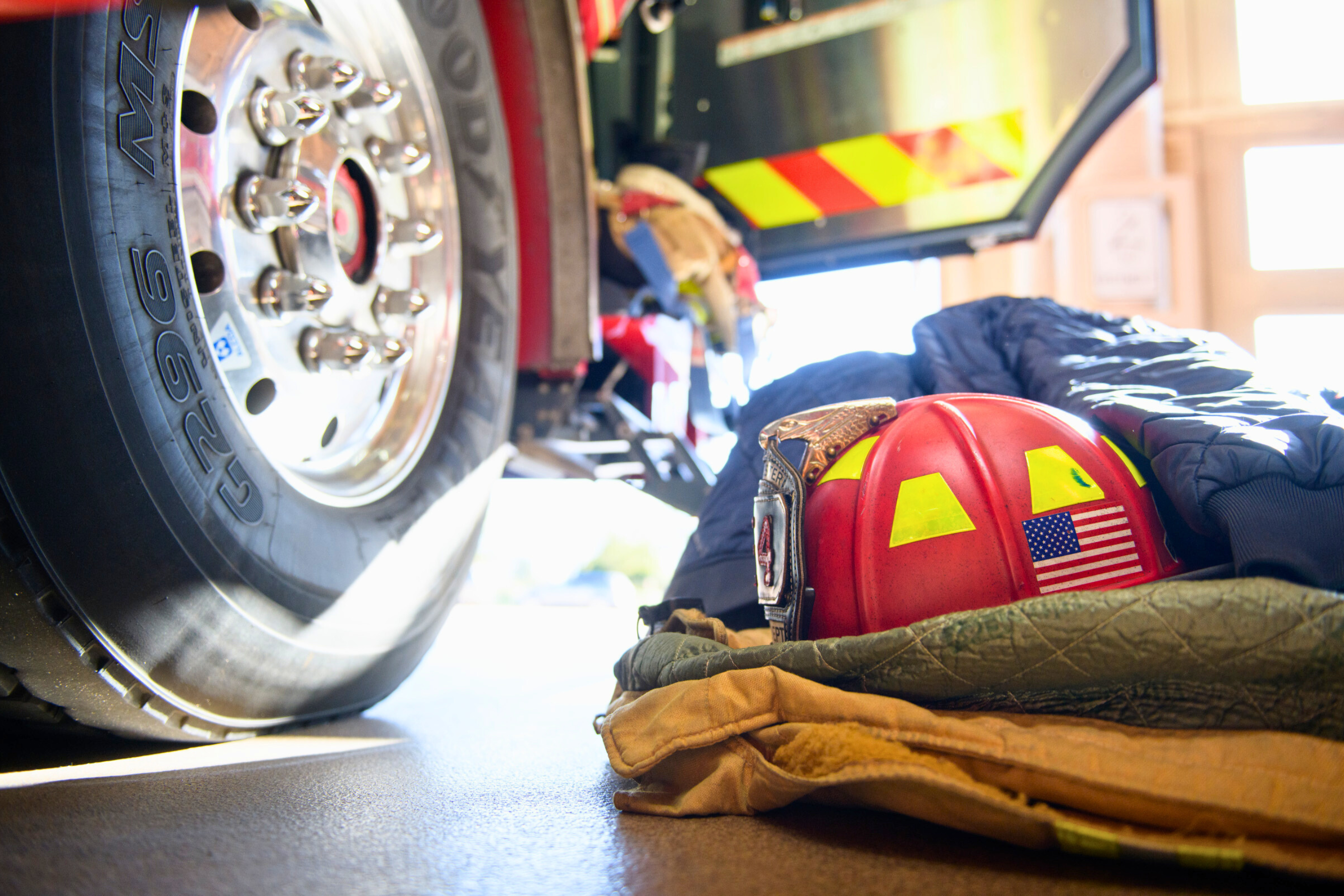 a firefighter helmet on a pile of folded turnout gear next to a fire engine wheel